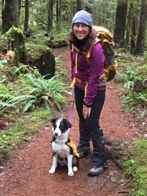 A woman with a backpack and a dog on a trail.