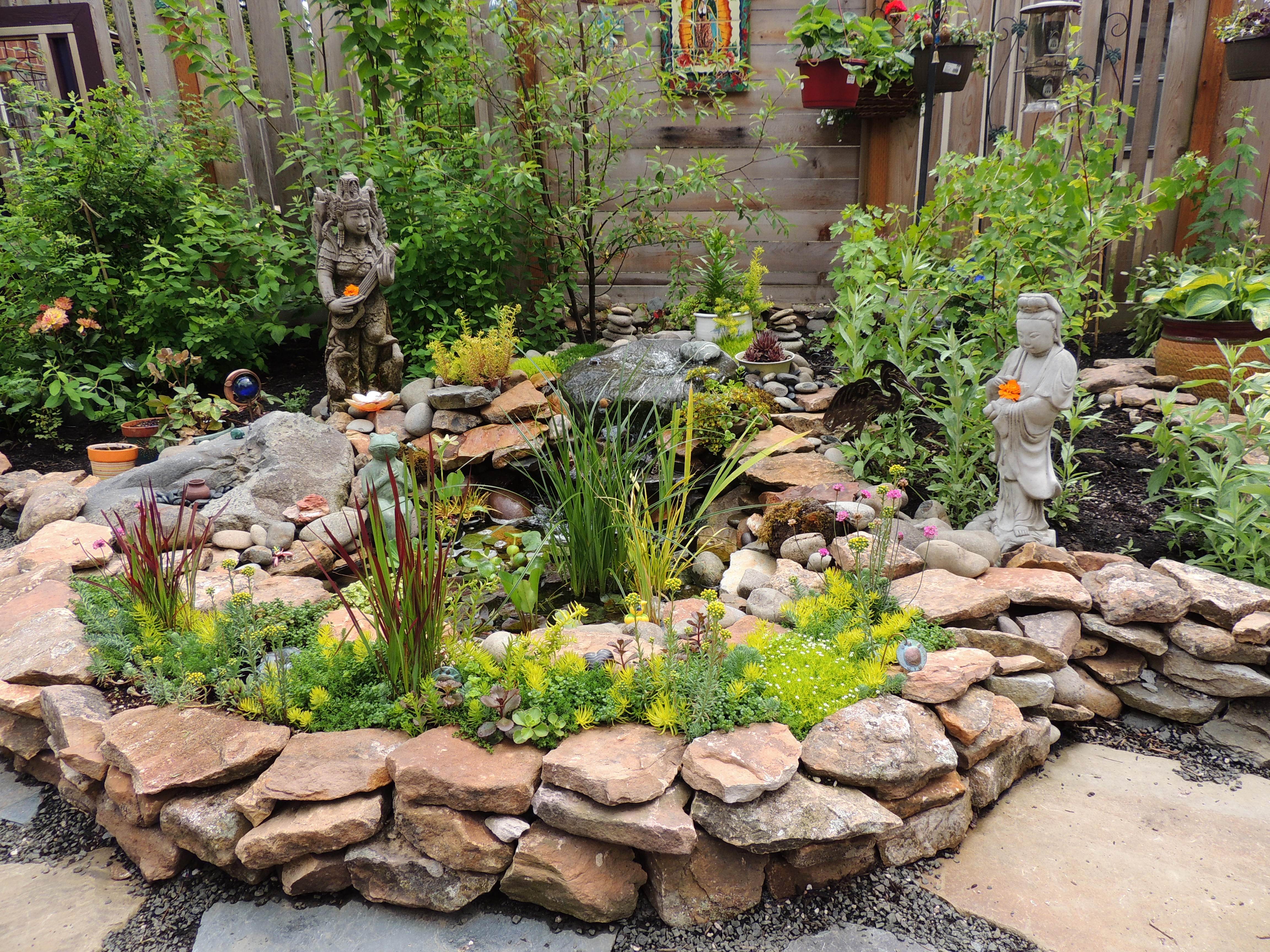 Garden. Pond lined with stones. Statues. Plants. Stone pavers.