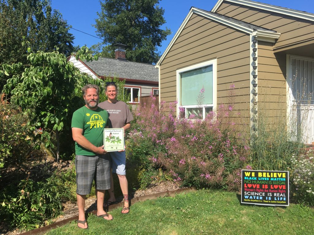 Two men standing in front of a house with a sign.