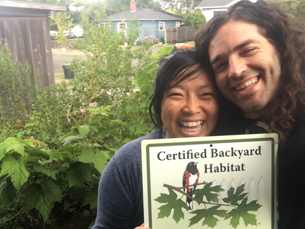 Two people holding up a sign that says certified backyard habitat.