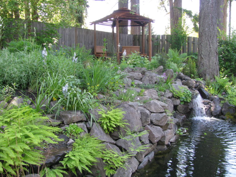 A pond in a backyard with rocks and a gazebo.