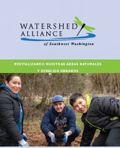 Three people are crouched down in a wooded area, wearing casual outdoor clothing and gloves. They are smiling at the camera. Above them is a logo for the Watershed Alliance of Southwest Washington with a dragonfly design.